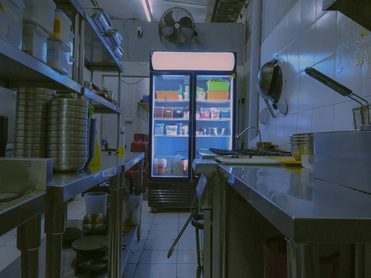 A restaurant kitchen after service, its two-door reach-in refrigerator still lit